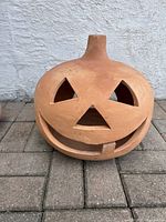Close-up of large terracotta Jack-o'-Lantern pumpkin face with carved eyes, nose, and mouth showing details of terracotta material and minor wear.