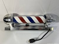 Front view of barber pole lamp on base showing red white blue spiral cylinder, metal housing and power cord