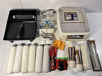 Overview of paint tray, roller covers, metal frames, safety goggles, and small accessories grouped on table.