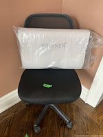 Black mesh office chair with Nikken pillow on seat in plastic wrap, showing minor wear and scratches