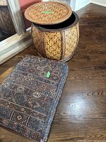 Photo showing woven basket drum with lid slightly lifted next to Moroccan henna Afghan pattern floor pillow on hardwood floor.