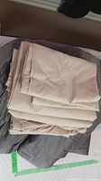 Folded beige king-size sheets placed on top of a grey weighted blanket on a bed.
