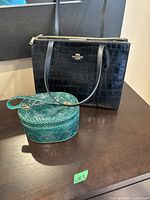 Front view of black croc-embossed Coach tote alongside green snakeskin-effect purse on tabletop