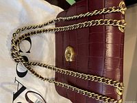 Front view of burgundy Coach croc-embossed leather bag with gold turn-lock and chain strap