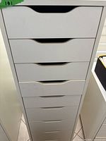 Front view of the tall white wood cabinet showing all nine drawers closed with signature cut-out handles.