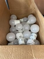 Box containing multiple white LED and spiral CFL light bulbs, some loose, visible from the top