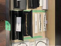 Five pieces of jewelry including four bracelets and one necklace, all displayed with original boxes on a table with light cardboard backing.