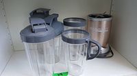 NutriBullet blender base unit with five clear plastic mixing jars in front, all with gray lids, one jar with handle