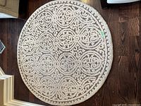 Full view of round rug showing the beige and brown ornate design on wooden floor