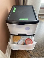Plastic organizer drawer with white translucent drawers and black top containing small food storage containers with red, yellow, and transparent lids