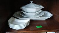 Full view of white ceramic serving pieces including platters, covered bowl, and side plates on a wooden shelf