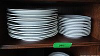 Stacks of plates showing 12 dinner plates on left and 12 side plates on right on wooden shelf