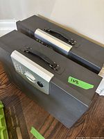 Pair of black and silver electronic safes shown side by side with keypad and handle on top visible.