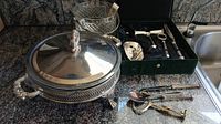Full view of silver service items including covered serving bowl, glass and silver ice bucket, and box with silver utensils