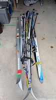 Top view of assorted skis and poles bundled together showing various brands and sizes.