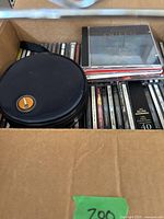 Top-down photo of box with CDs stacked, shows 'Classic Queen' CD and black round CD case on top.