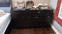 Front view of the dark wood dresser with items on top and closed drawers.