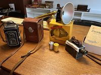 Group shot showing Foth-Flex camera, leather case, Kodak Photo Flasher kit and brass monocular on wood table