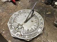 Top view of the sundial showing Roman numerals, motto, and hourglass wing motif