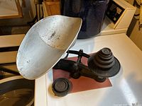 Side view of antique iron and brass weigh scale with removable metal pan for goods being weighed, showing the scale arm and pan shape and size.