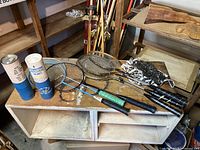 Full badminton set displayed on white shelf consisting of eight rackets, net rolled and tied, and two shuttlecock containers.