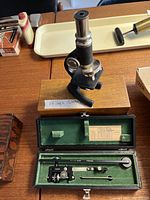 Photo showing small antique microscope on wooden base with note of size and open case with Keuffel & Esser Planimeter inside.