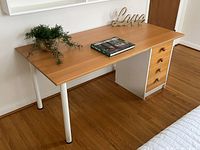 Full front side view of desk showing four drawer cabinet with pine fronts and white desk legs and frame, beechwood top with items on top.