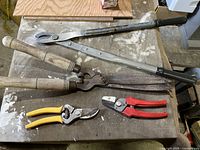 Full set of garden pruning tools on a workbench showing all four tools.