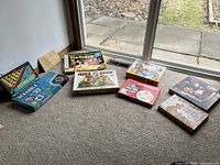 Table with nine boxed kids games including Scrabble for Juniors, Flying Hats, Twister, Hide and Seek, Dont Break the Ice, Spirograph, Pin the Tail on the Donkey, and two puzzles.