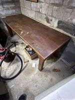 Full view of the large solid wood work table showing the stained tabletop and heavy solid legs.
