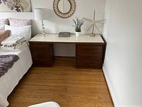 Full view of mid-century desk with two dark brown chest of drawers and cream top surface, positioned against cream wall and adjacent to bed