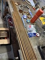 Eight copper pipes of varying lengths laid out on a bench with plumbing fittings and tools scattered around.