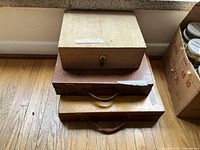 Three stacked wooden boxes of varying sizes on a floor under a window sill, unopened, showing natural wood finish and carry handles.
