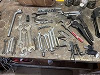 Wide shot showing a variety of wrenches including adjustable, pipe wrench, Allen keys, and socket wrench pieces laid out on a workbench.