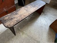 Vintage solid pine bench with rounded front corners seen from a side angle showing worn dark finish and angled legs.
