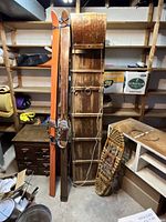 Photo showing pair of vintage downhill skis, wooden toboggan, and a pair of snowshoes against shelving in a storage area.