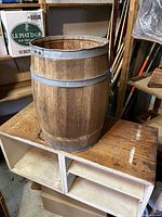 Full view of medium-brown wooden barrel with metal bands on top of a wooden cubby shelf.