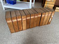 Twelve vintage wooden file boxes arranged in a row on carpet, showing consistent size and shape, with attached paper labels on the side.