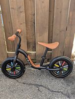 Side view of the black Chillafish Buzzi balance bike with brown saddle and grips, colorful spoke accents on wheels