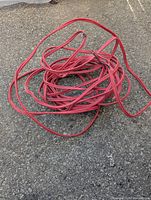 Coiled red electrical wire laid on the ground showing the full length and condition of the wire.