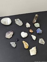 Overview of all 15 assorted crystals on a black surface, variety of sizes and colors shown including polished and rough specimens