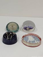 Four mid-century modern style paperweights with varied designs displayed on flat surface.