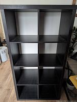 Front view of black 8-cube storage shelf showing 8 equal compartments, visible wear and scratches.