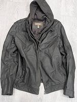 Front view of black leather jacket with attached black hoodie laid flat showing overall design and condition.