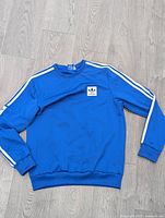 Front view of royal blue Adidas sweatshirt with white stripes on sleeves and logo patch on chest