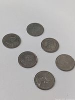 Top-down photo showing six Canadian silver dollar coins laid out in a circular formation on a white surface.