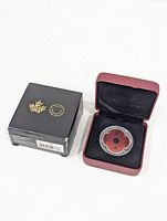 Maroon hinged display box with black interior lining holding the coin inside a clear protective plastic case showing red poppy design with black center.