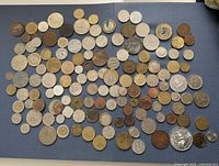 Overview photo showing a large assortment of mixed world coins laid out on a blue surface.
