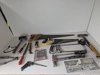 Image showing a spread of various construction hand tools including hammers, saws, screwdrivers, putty knives, and measuring tape on a white surface.