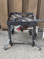 Front angled view of the propane burner showing the metal frame, burner area, and propane hose with regulator and control knob.